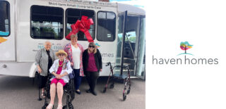 Haven Homes residents and staff stand proudly in front of their new bus, decorated with a large red bow, symbolizing the community's excitement for new adventures.